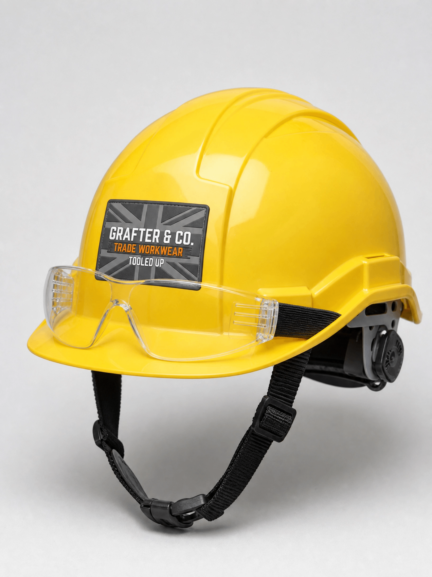 Grafter & Co. yellow hard hat with clear safety specs attached on a plain background