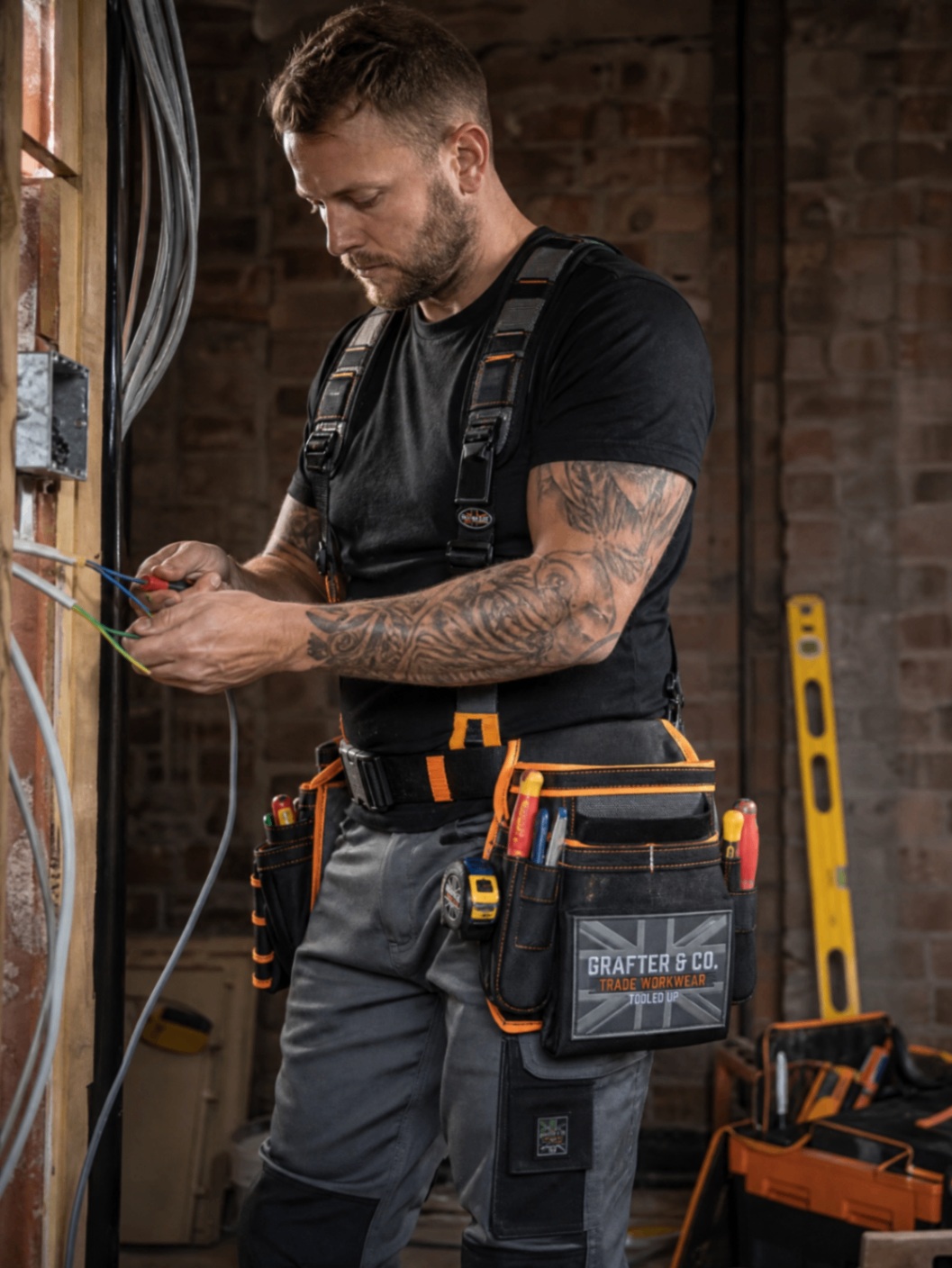 Electrician wearing a Grafter & Co. tool belt and braces while wiring on a first-fix site