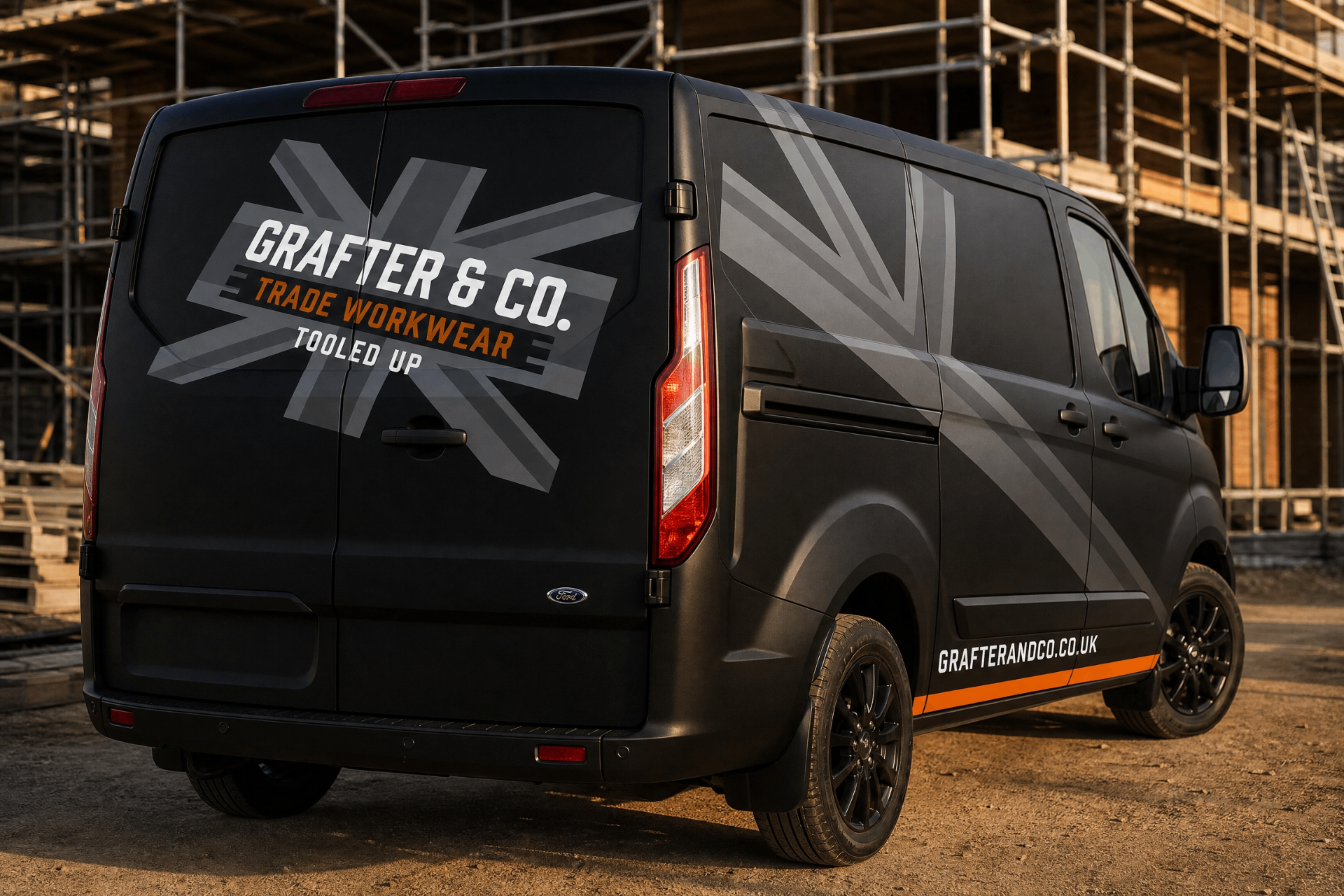Matte black Ford Transit Custom van with grey union jack livery, Grafter & Co. Trade Workwear logo and orange side stripe parked at a scaffolded build site